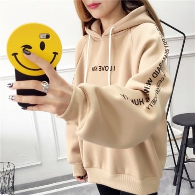 Woman taking a mirror selfie in an oversized beige hoodie with sleeve lettering, product shot