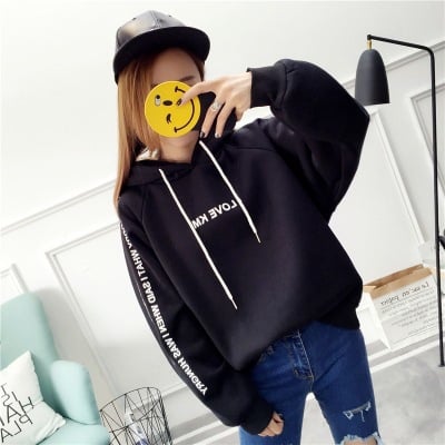 Woman taking a mirror selfie in an oversized black hoodie with sleeve lettering, front view