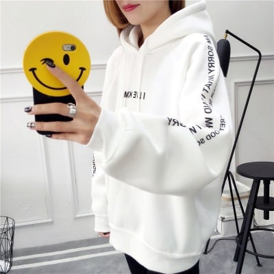 Woman taking a mirror selfie in an oversized white hoodie with sleeve lettering on a white background