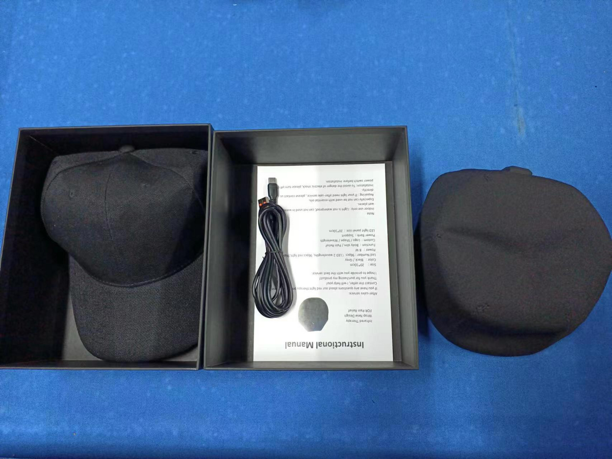 Boxed red light therapy cap with charging cable and manual, front view