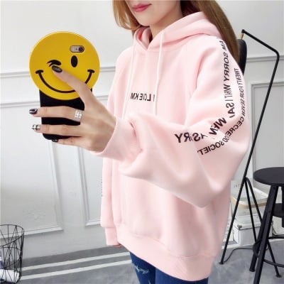 Woman taking a mirror selfie in an oversized pink hoodie with sleeve lettering shown upright