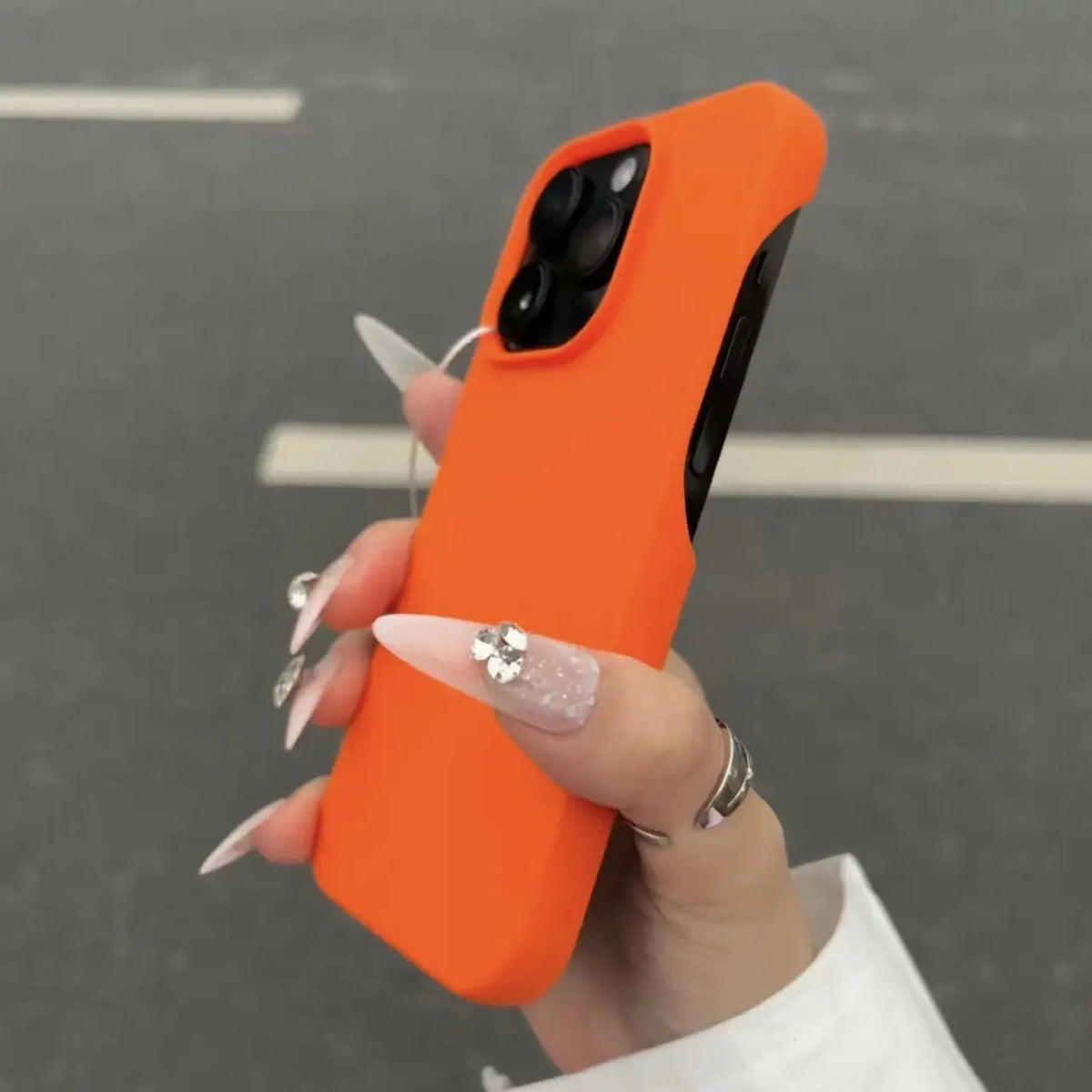 Hand holding a orange half-pack graphite phone case outdoors, catalog shot