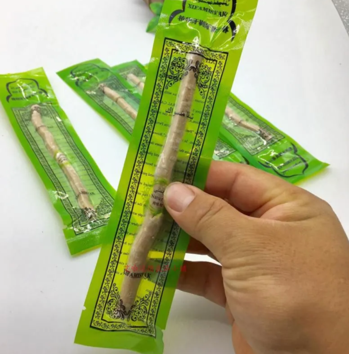 Hand holding a sealed miswak tooth cleaning stick in green packaging