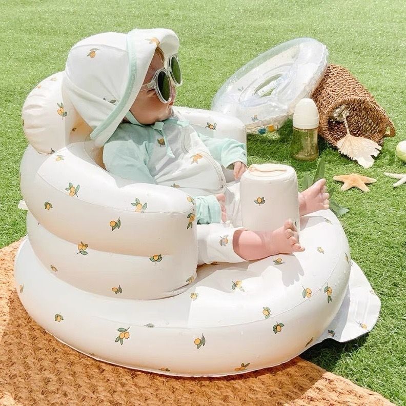 Baby in sunglasses sitting in an inflatable baby chair outdoors on grass