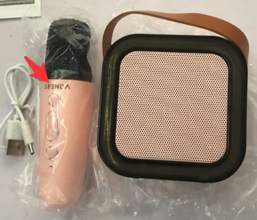 Unboxed karaoke speaker with pink microphone and USB charging cable