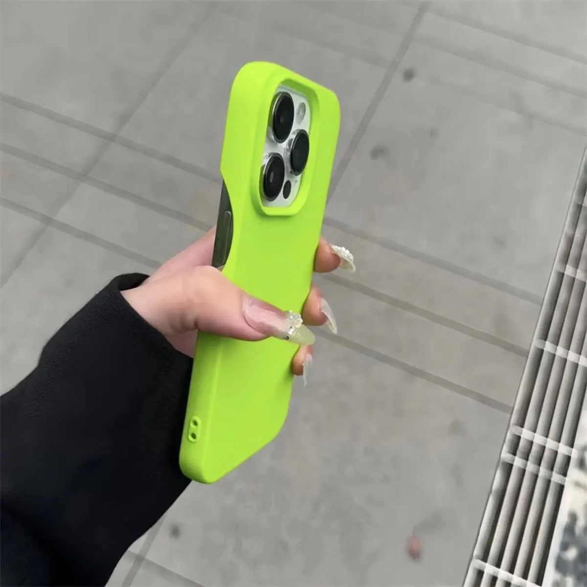 Hand holding a lime green half-pack graphite phone case outdoors against white